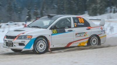 Mitsubishi Lancer Evolution 5 berwarna hitam melaju kencang di jalan kota, menonjolkan desain sport dan performa